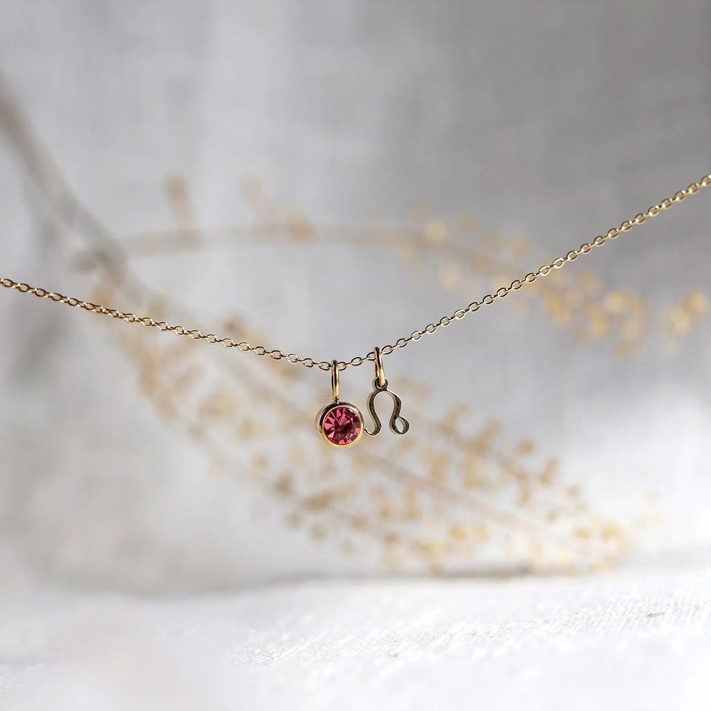 Collier "Mon identité" en acier doré, avec signe Lion et pierre rose, délicatement suspendu sur une chaîne fine.