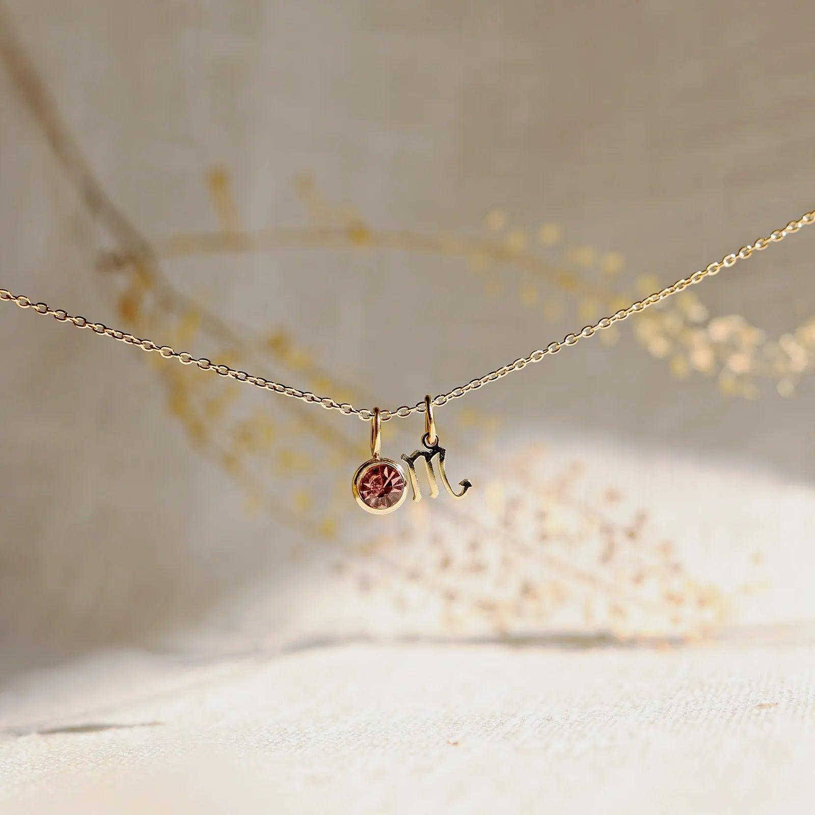 Collier "Mon identité" en acier doré, avec signe Scorpion et pierre rose, délicatement suspendu sur une chaîne fine.