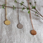 Collier "Reflet" avec médaille ronde personnalisé en acier inoxydable, posé sur un tissu beige texturé.