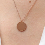Collier "Reflet" avec médaille ronde personnalisé en acier inoxydable rosé, porté autour du cou.