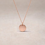 Collier "Reflet" avec médaille ronde personnalisé en acier inoxydable or rose, posé sur un fond beige texturé