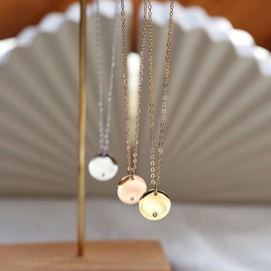 Vue d'ensemble du collier personnalisable "Lumineuse", orné d'une médaille ronde brillante, disponible en acier doré, rosé ou argenté.