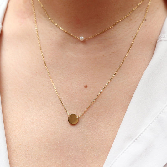 Double collier "Je me choisis" composé d'une perle et d'un médaillon en acier doré, porté autour du cou. 