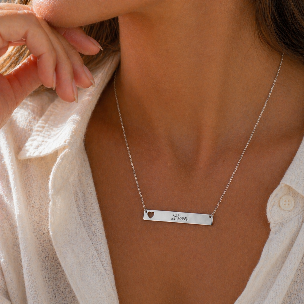 Collier personnalisable cœur argenté, gravé au nom de Léon, portée sur une femme en chemise blanche– Douceur Visée Bijoux
