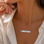 Collier personnalisable cœur argenté, gravé au nom de Léon, portée sur une femme en chemise blanche– Douceur Visée Bijoux