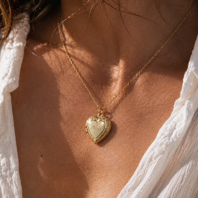 Zoom sur le collier Précieux, médaillon cœur en acier doré avec photo souvenir à personnaliser et gravure sur le devant du cœur,  posé sur un fond beige texturé.