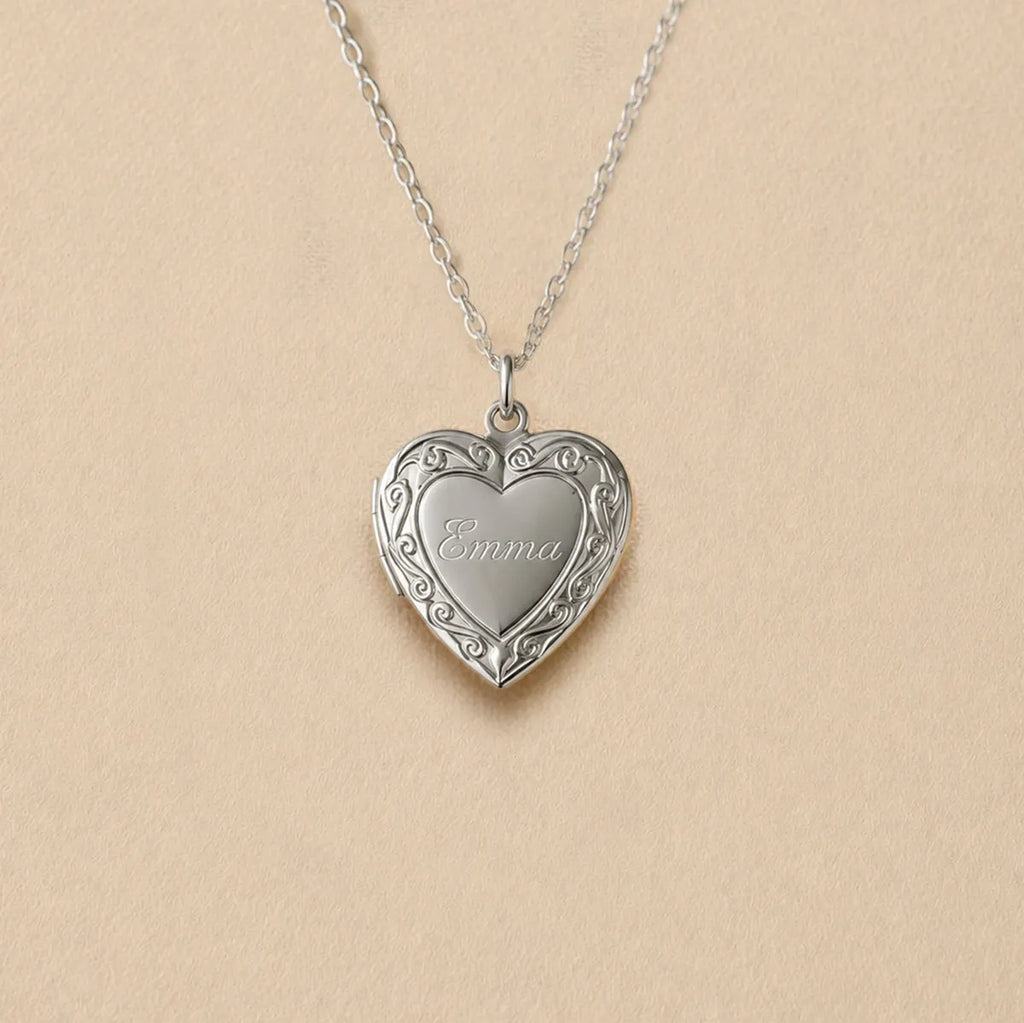 Zoom sur le collier Précieux, médaillon photo cœur en acier argenté avec gravure prénom et  photo souvenir à personnaliser, posé sur un fond beige texturé.