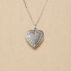 Zoom sur le collier Précieux, médaillon photo cœur en acier argenté avec gravure prénom et  photo souvenir à personnaliser, posé sur un fond beige texturé.