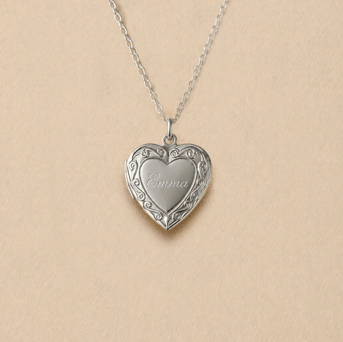 Zoom sur le collier Précieux, médaillon photo cœur en acier argenté avec gravure prénom et  photo souvenir à personnaliser, posé sur un fond beige texturé.