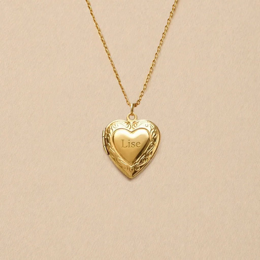 Zoom sur le collier Précieux, médaillon photo cœur en acier doré avec gravure prénom et  photo souvenir à personnaliser, posé sur un fond beige texturé.