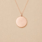 Collier "Reflet" avec médaille ronde personnalisé en acier inoxydable couleur or rose, posé sur un fond beige texturé