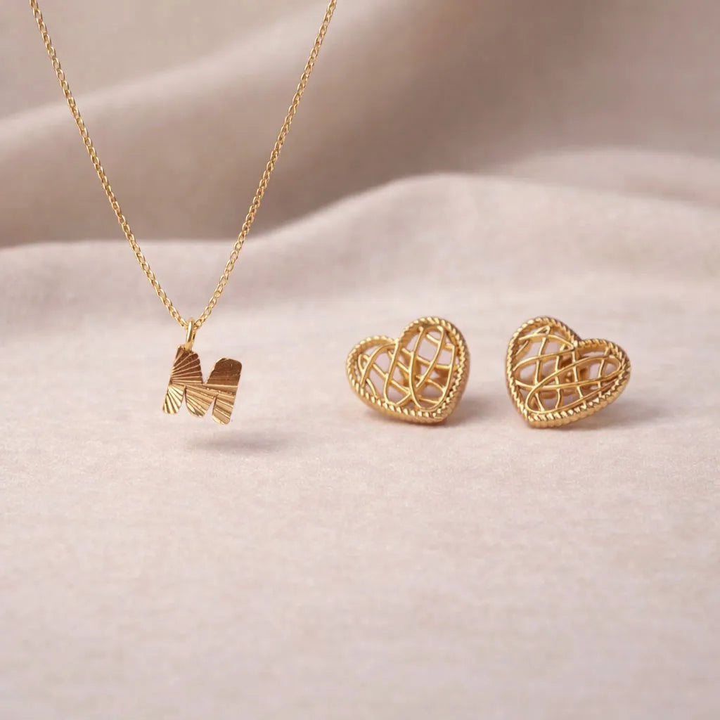 Coffret Évidence – Collier initiale & boucles cœur entrelacées Visée, posé sur un fond beige texturé.