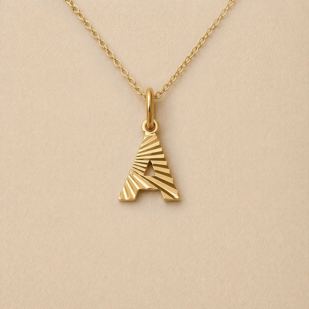 Collier lettre initiale A striée doré Grace, photographié sur fond beige texturé.