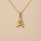 Collier lettre initiale A striée doré Grace, photographié sur fond beige texturé.