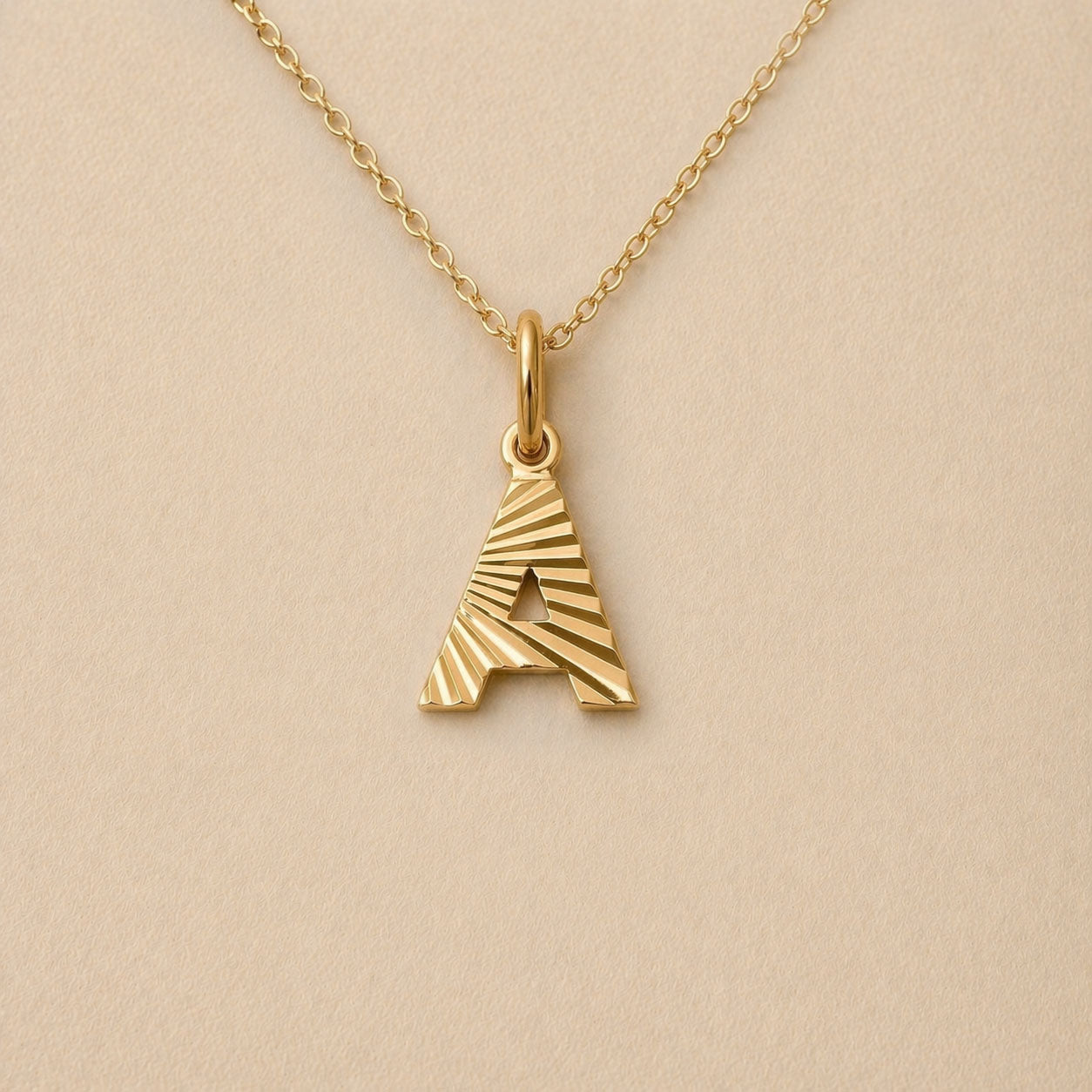 Collier lettre initiale A striée doré Grace, photographié sur fond beige texturé.