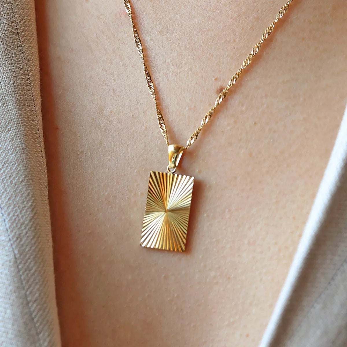 Collier Eclat en acier doré avec pendentif rectangulaire gravé de rayons, personnalisable au verso, porté autour du cou.