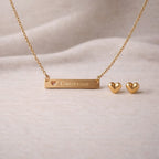 Collier personnalisé doré Douceur et les boucles d'oreille Doux en acier inoxydable doré, posé sur un fond beige texturé.