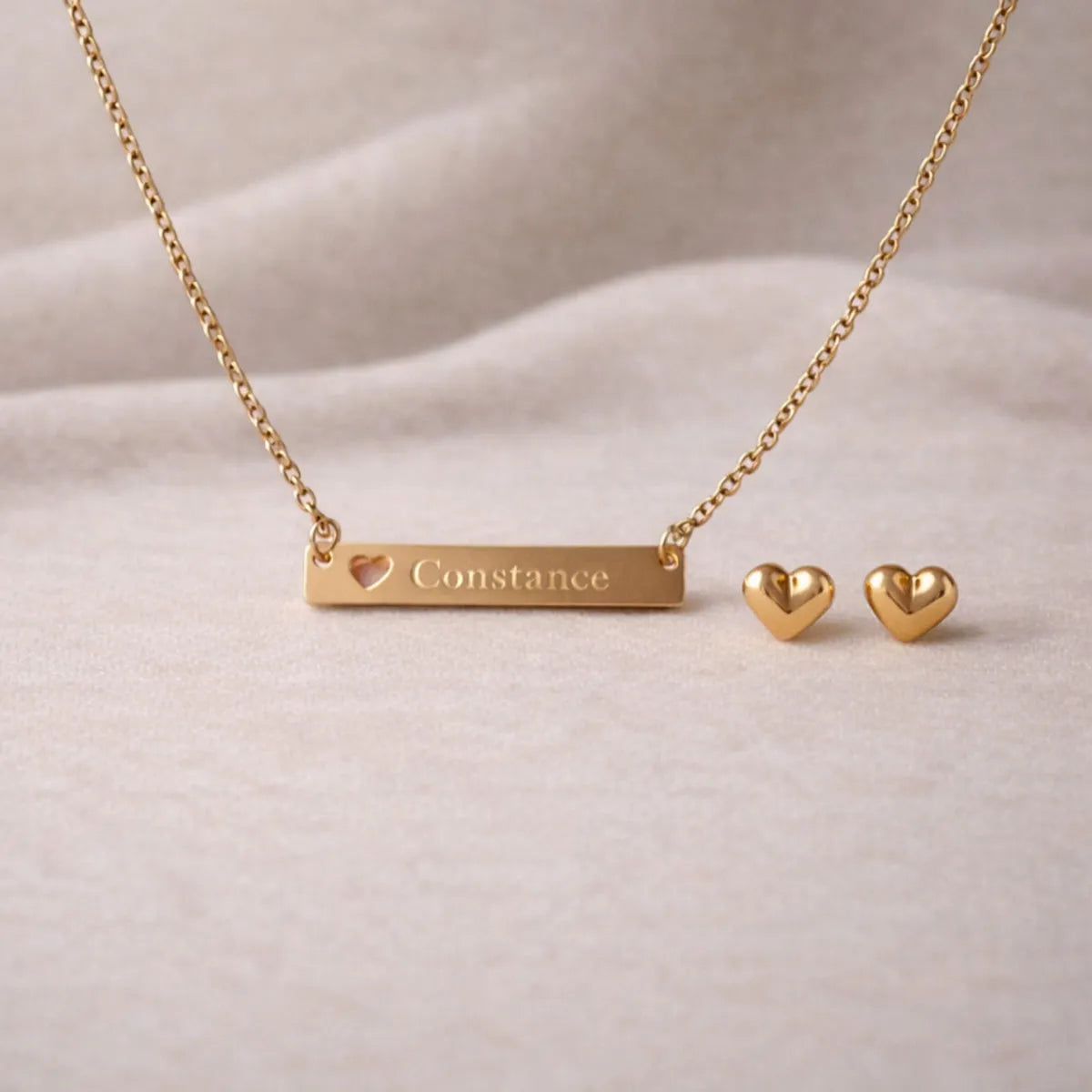 Collier personnalisé doré Douceur et les boucles d'oreille Doux en acier inoxydable doré, posé sur un fond beige texturé.