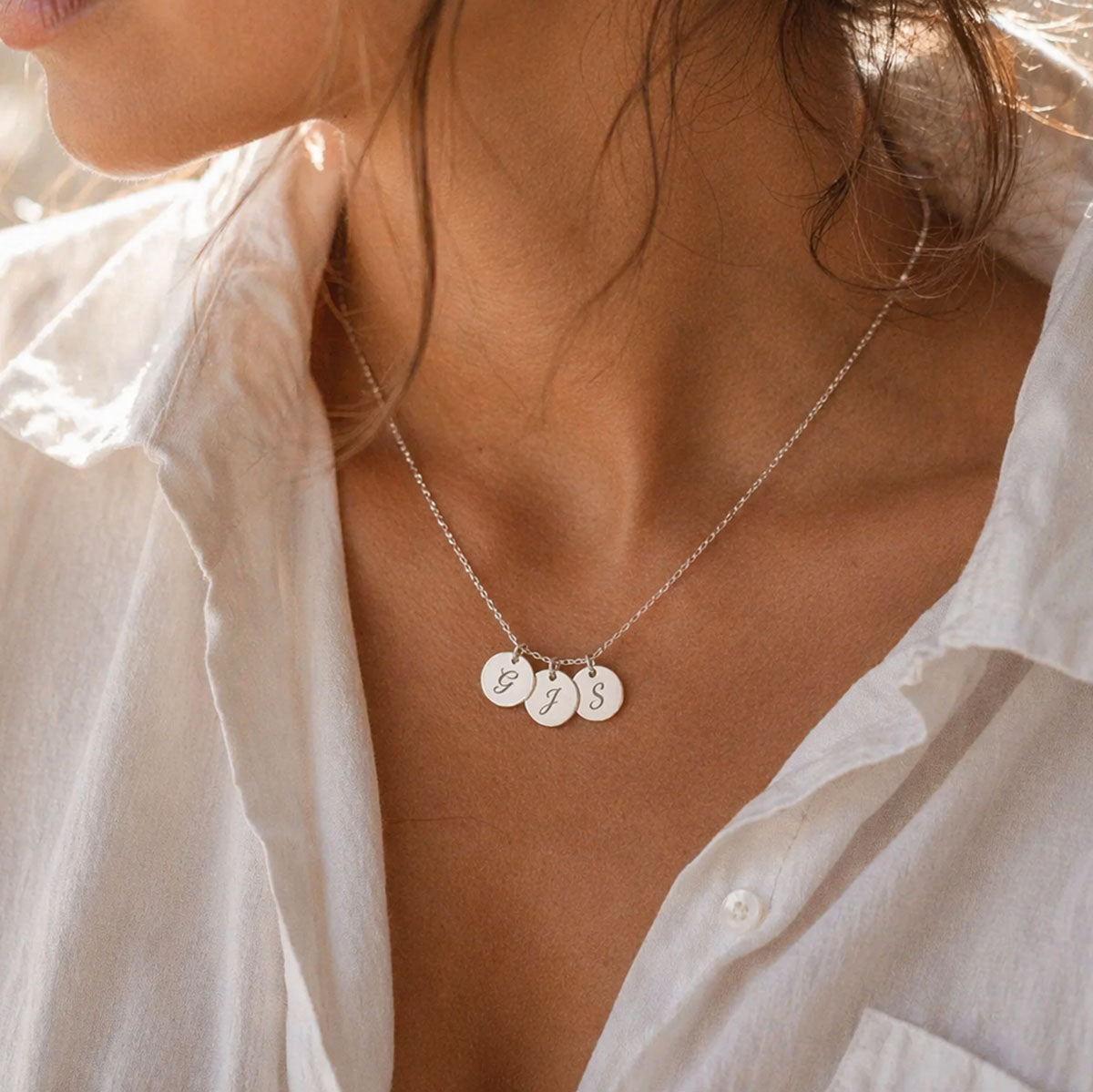 Collier Inspiration en acier inoxydable argenté avec trois médaillons personnalisables gravés G, J et S, porté par une femme en chemise blanche — Visée