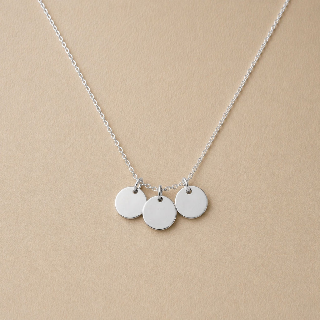 Collier "Inspiration" en acier inoxydable argenté, composé de trois médaillons personnalisables, présenté sur un fond beige texturé.