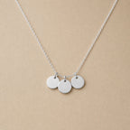 Collier "Inspiration" en acier inoxydable argenté, composé de trois médaillons personnalisables, présenté sur un fond beige texturé.