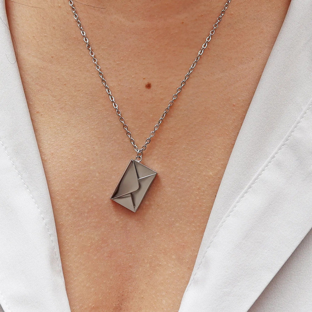 Collier "Nid secret", pendentif en forme d'enveloppe argentée fermée, porté autour du cou.