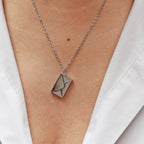 Collier "Nid secret", pendentif en forme d'enveloppe argentée fermée, porté autour du cou.