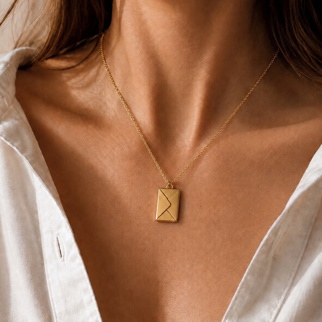 Collier "Nid secret", pendentif en forme d'enveloppe dorée fermée, porté autour du cou.