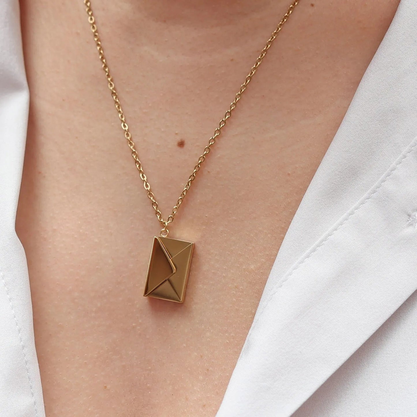 Collier "Nid secret", pendentif en forme d'enveloppe dorée fermée, porté autour du cou.