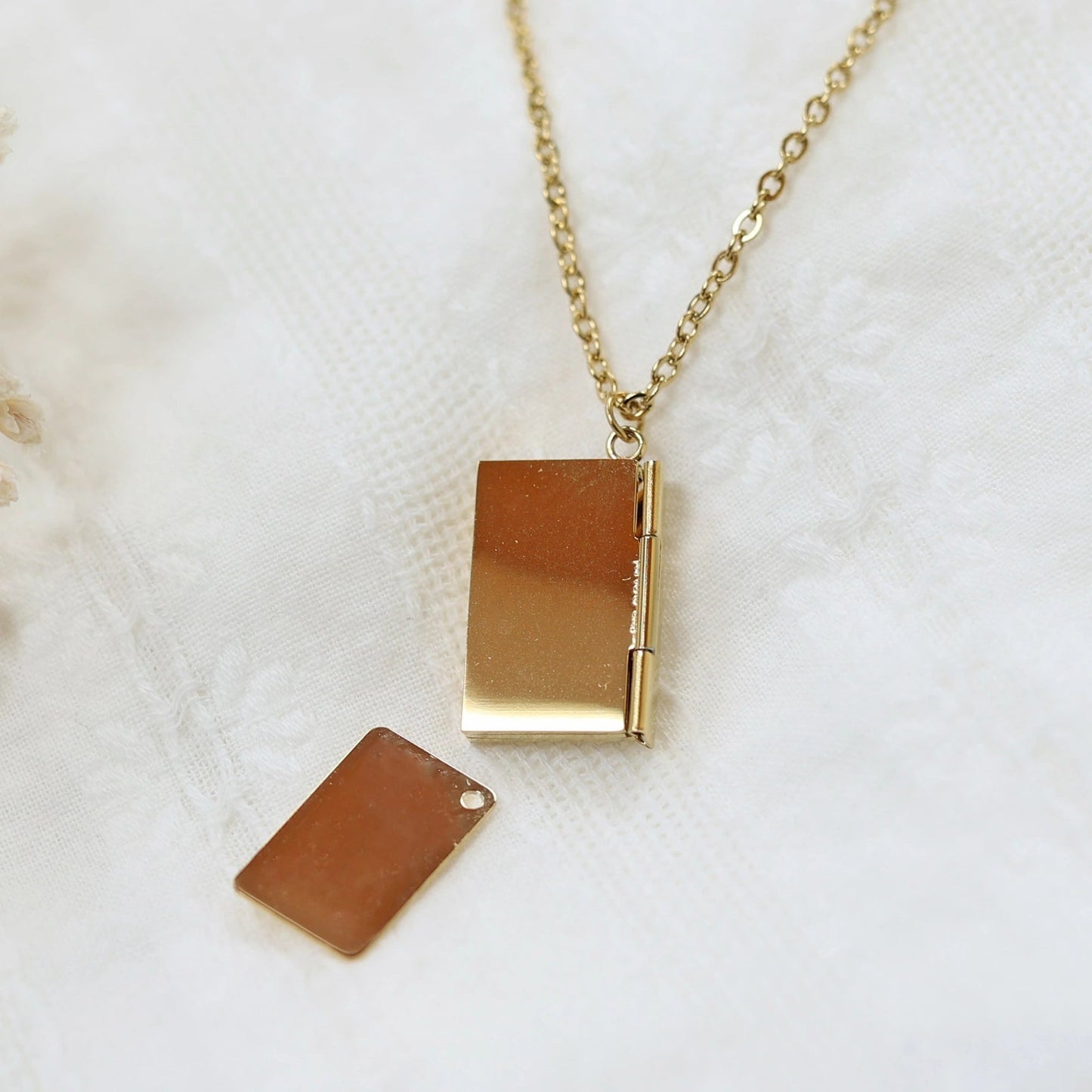 Collier "Nid secret", pendentif en forme d'enveloppe dorée ouverte, dévoilant un message, posé avec soin sur un fond beige texturé.