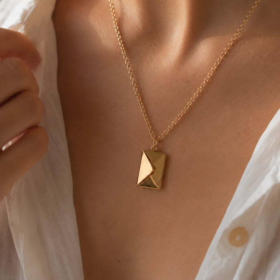 Collier "Nid secret", pendentif en forme d'enveloppe dorée fermée, porté autour du cou.