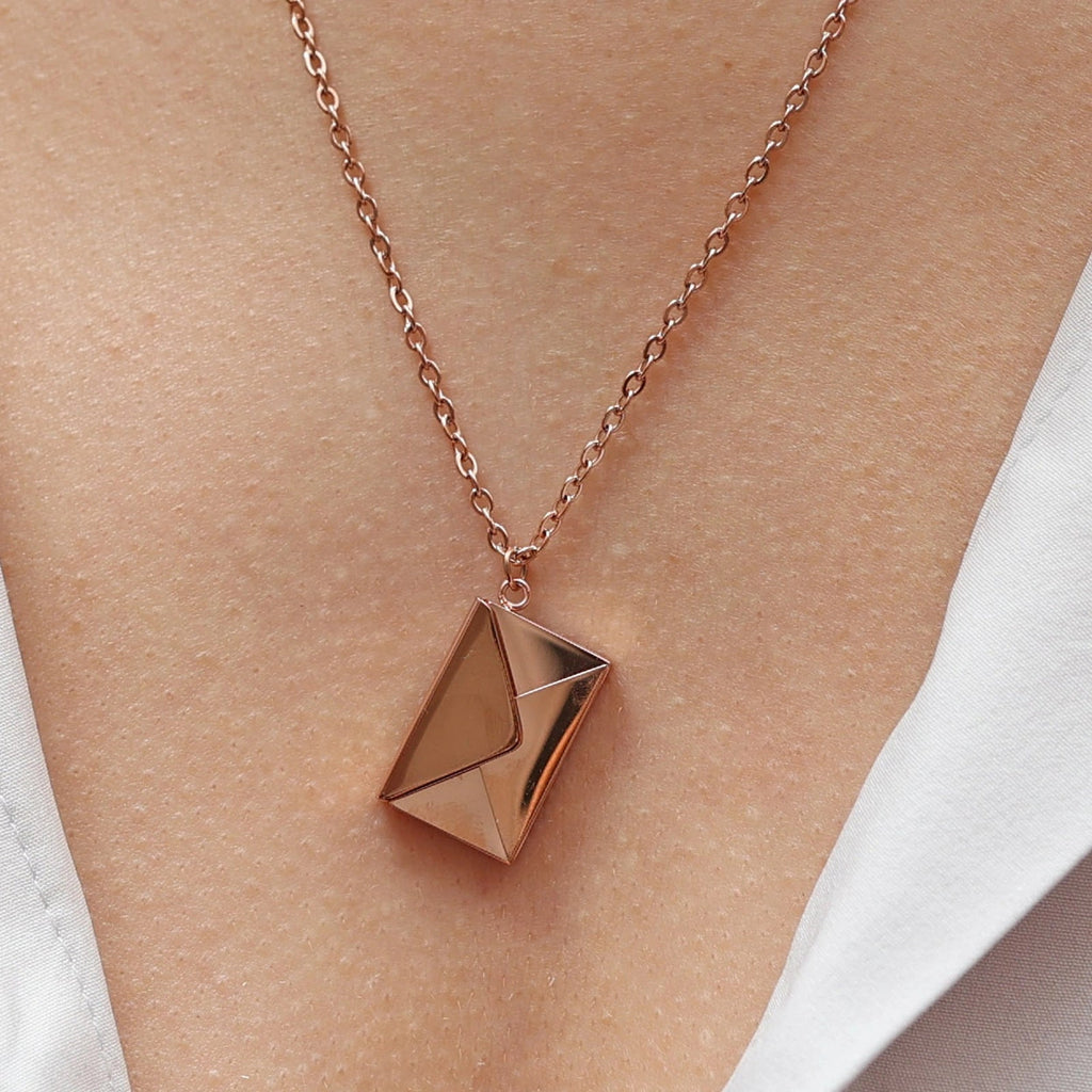 Collier "Nid secret", pendentif en forme d'enveloppe rosé fermée, porté autour du cou.