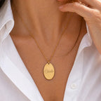 Zoom sur le collier "Tendresse", pendentif ovale personnalisable en acier inoxydable doré, porté autour du cou, avec chemise blanche