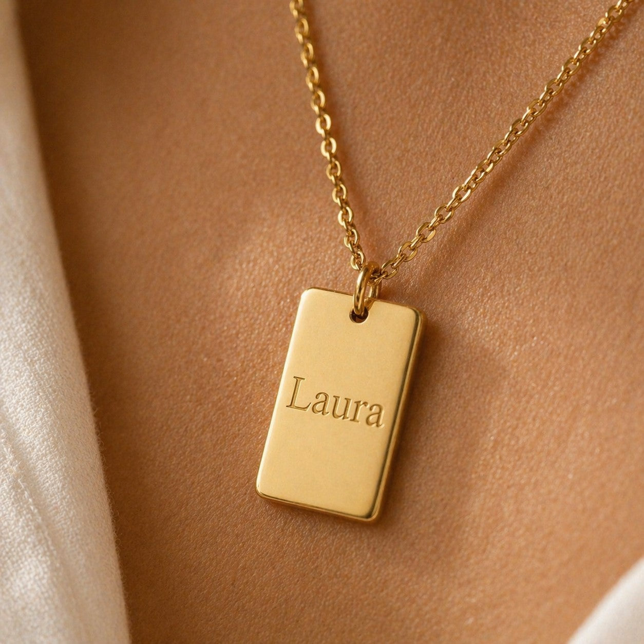 Zoom sur le collier Tracé en acier inoxydable doré, avec médaille rectangulaire gravé du prénom de Laura, porté autour du cou. 