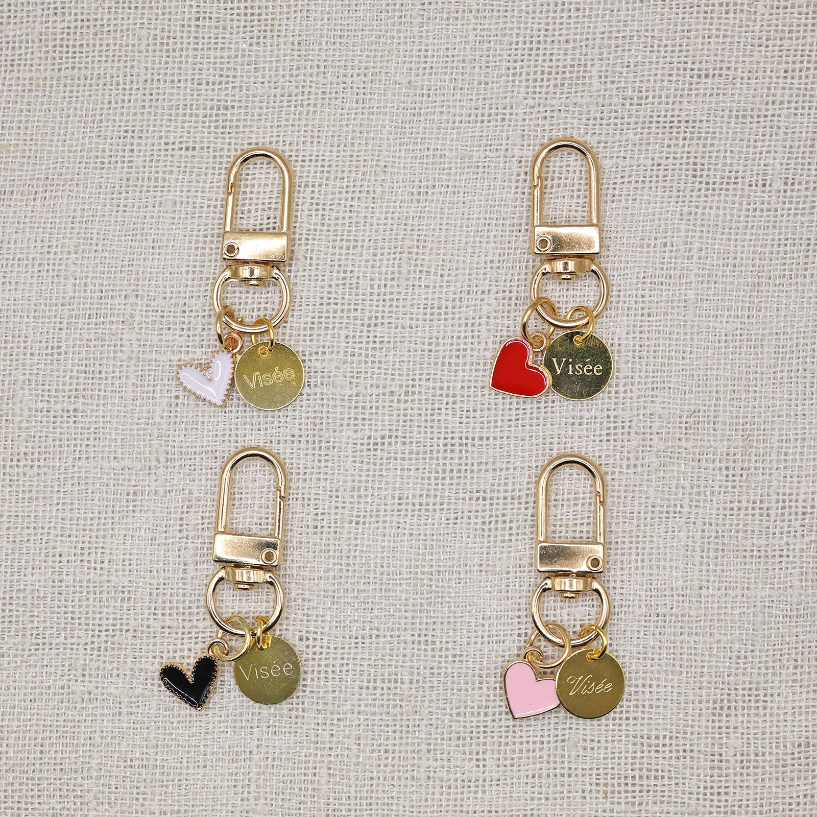 Quatre porte-clés avec médaillon Visée et pendentif coeur en acier inoxydable, sur fond beige.