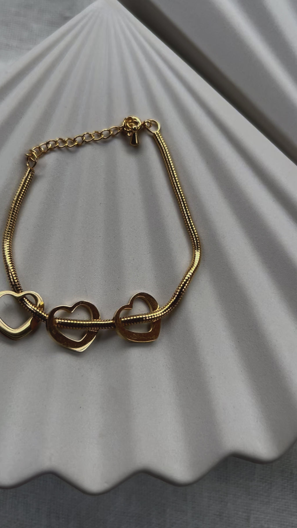 Vidéo du bracelet "Emotive" en acier doré, orné de trois cœurs mobiles, posé sur un fond beige texturé.