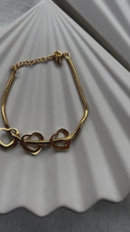 Vidéo du bracelet "Emotive" en acier doré, orné de trois cœurs mobiles, posé sur un fond beige texturé.
