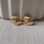 Vidéo des boucles d’oreilles torsadées Métamorphose en acier inoxydable doré, posées sur un tissu beige texturé.