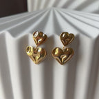 Boucles d’oreilles pendantes double cœur en acier inoxydable doré, au design ondulé et moderne, parfaites pour un look audacieux et élégant.