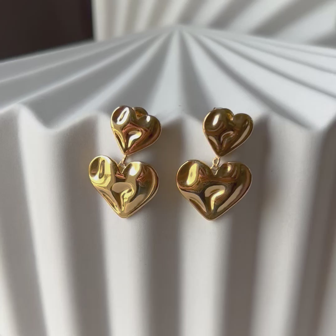 Boucles d’oreilles pendantes double cœur en acier inoxydable doré, au design ondulé et moderne, parfaites pour un look audacieux et élégant.
