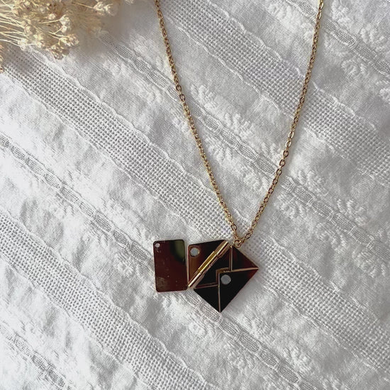 Vidéo du Collier "Nid secret", pendentif en forme d'enveloppe dorée ouverte, dévoilant un message, posé avec soin sur un fond beige texturé.