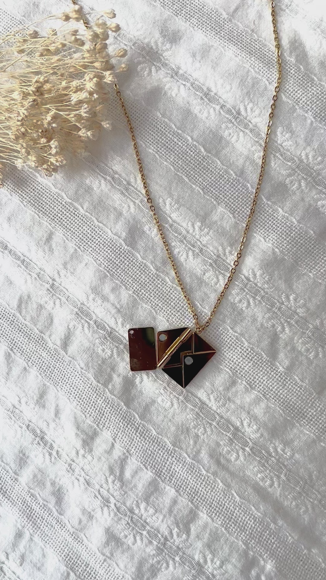 Vidéo du Collier "Nid secret", pendentif en forme d'enveloppe dorée ouverte, dévoilant un message, posé avec soin sur un fond beige texturé.
