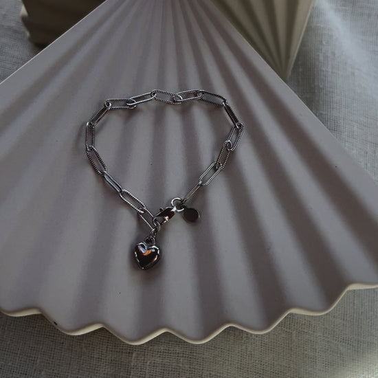Vidéo du bracelet Valeur acier inoxydable argenté, avec breloque cœur personnalisable, posé sur un fond beige texturé.