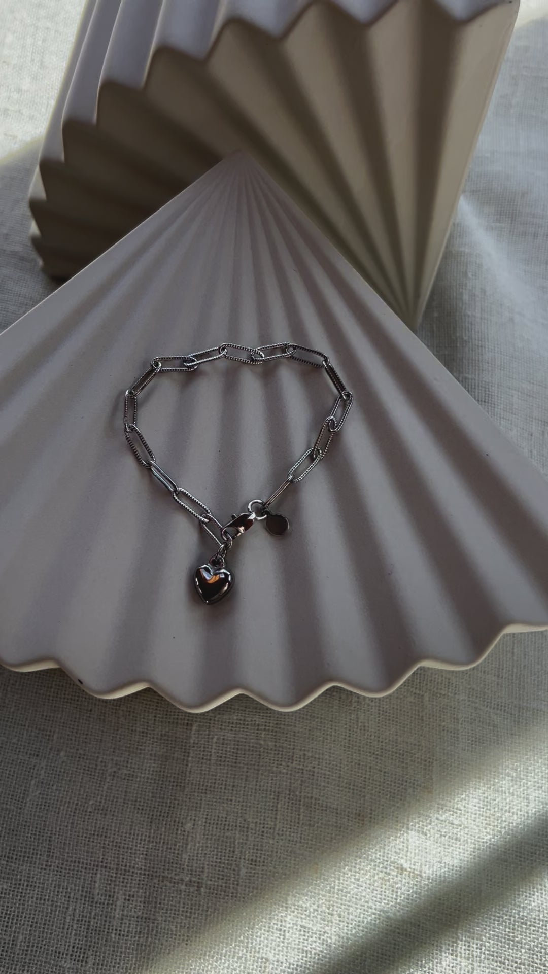 Vidéo du bracelet Valeur acier inoxydable argenté, avec breloque cœur personnalisable, posé sur un fond beige texturé.