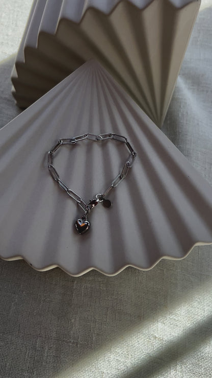Vidéo du bracelet Valeur acier inoxydable argenté, avec breloque cœur personnalisable, posé sur un fond beige texturé.