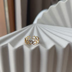 Vidéo de la bague "Unité" réglable en acier doré, composée de cœurs entrelacés, posé sur un support beige texturé.