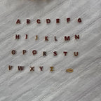 Vidéo de l'ensemble des pendentifs lettres dorées en acier inoxydable, soigneusement alignés  sur un tissu beige texturé.
