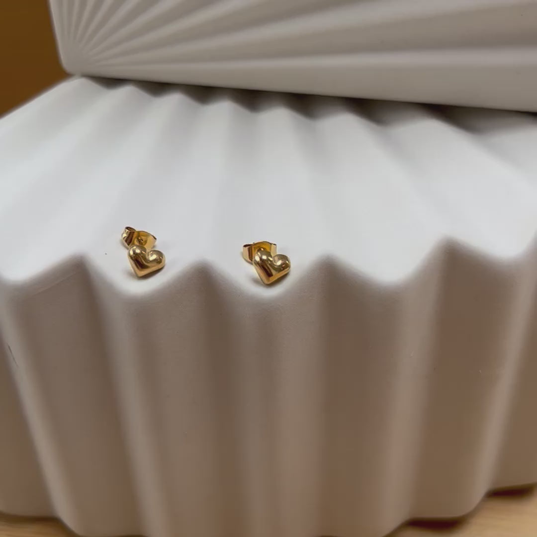 Vidéo des boucles d'oreilles "Tendre discrétion" de Visée, en forme de cœur en acier doré, posées sur un fond beige texturé.