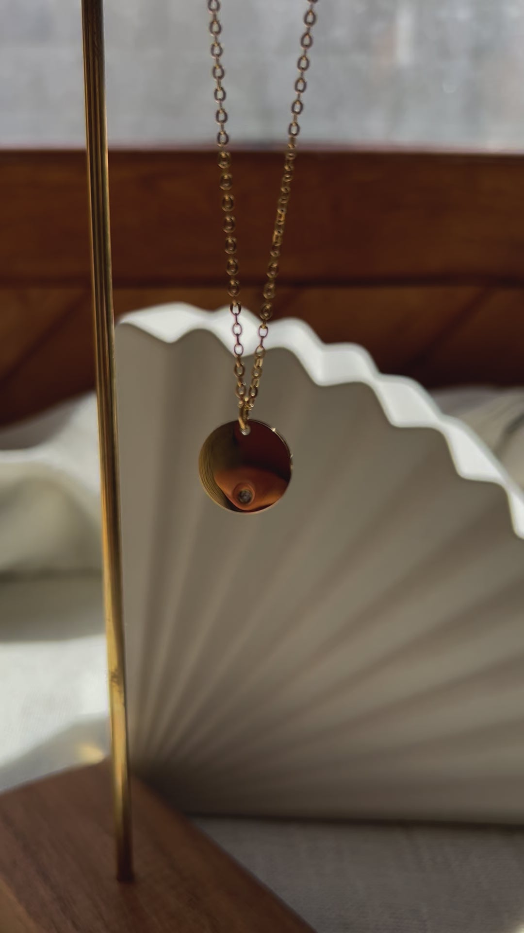 Vidéo du collier personnalisable "Lumineuse", orné d'une médaille ronde brillante en acier doré, posé sur un fond beige texturé.