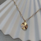Vidéo du collier "Energie", pendentif rond strié personnalisable en acier doré, posé sur une structure beige.